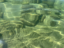 Ocean Background. Sea Water Close Up. Transparent Water, Stones On A Sandy Bottom. Glare, Reflection Of Sun On The Water Surface. Clear Turquoise Water. Ecology, Environment. Tropical Beach. Travel.