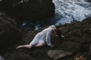 beautiful young woman lying on rocky coast with cracks on rocky surface unaltered