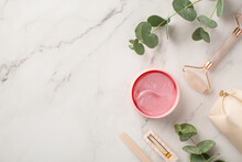 Skincare Beauty Concept. Top View Photo Of Pink Barrette Nail File Rose Quartz Roller Pink Eye Patches Cosmetics Bag And Eucalyptus On White Marble Background With Copyspace