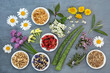 Healing herbs and flowers used in herbal plant medicine in bowls and loose. Alternative health care natural flower remedy concept. Top view, flat lay on mottled grey background.