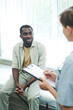 © Mediaphotos - Young Afro-American patient sitting on couch in emergency room and talking to doctor