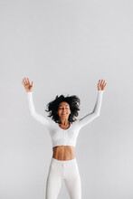 A Happy Woman In White Sportswear Bounces On A White Background. The Girl, Jumping, Raised Her Hands Up In The Gym