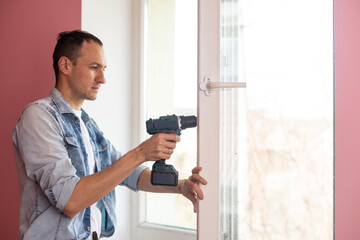 Wall Mural - Handyman using a cordless screwdriver to install a window handle. Qualified worker services, home repair and renovation.