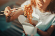 © EdNurg - Happy Asian girl holds chopsticks and eats wok tasty noodles from a takeaway paper box. Street and fast food concept