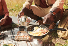 Close-up Of Unrecognizable Black Man In Smartwatch Cooking Eggs On Burner And Putting It In Metallic Bowl Outdoors