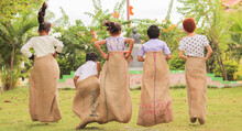 Back View Shot Of Group Of Childrens Playing Potato Sack Jumping Race Game At Park During Summer Camp - Concept Of Childhood Physical Activities And Holiday Nations.