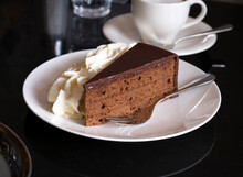 Piece Of Famous Sachertorte Chocolate Cake With Apricot Jam Of Austrian Origin Served With Whipped Cream