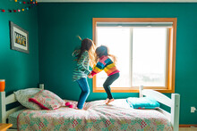 Two Young Sisters Hold Hands And Jump On A Bed