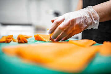 Close-up of hand sushi chef in gloves slices fresh salmon fish fillet at sushi bar.