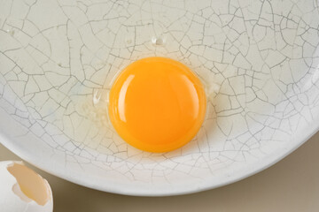 Broken egg with a yellow yolk in a white plate. Shallow depth of field