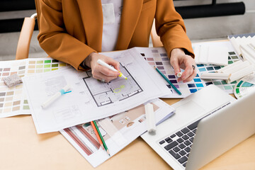 Woman architect working on interior renovation in workplace. Designer choosing color samples according to the visualization and blueprints of the project. Architecture and interior design concept.