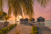 Fantastic Island Beach And Sunset Sky With Palm Tree Leaves. Luxury Tropical Beach Landscape, Wooden Jetty Into Over Water Villas, Bungalows Amazing Scenic. Vacation Resort, Exotic Hotel Landscape