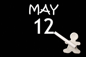 Wall Mural - A small white plasticine man writing the date 12 May on a black board. Business concept. Education concept.