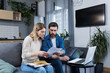 © Liubomir - Husband and wife, young family working together on home finances, arguing bills, using laptop, sitting on sofa at home