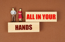 On Wooden Blocks With The Inscription - ALL IN YOUR HANDS, There Are Miniature Figures Of People.