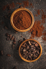 Sticker - Cocoa beans and cocoa powder in wooden bowls on black table.