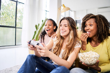 Wall Mural - Group of young female multiracial young friends play video games together at home. Only women gaming and eating popcorns. 