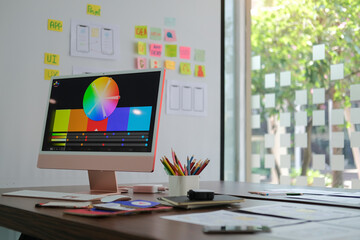 Creative designer workplace with modern computer, paperworks and stationery on wooden table.