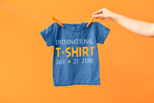 Woman Hanging T-shirt On Laundry Line Against Color Background. International T-Shirt Day