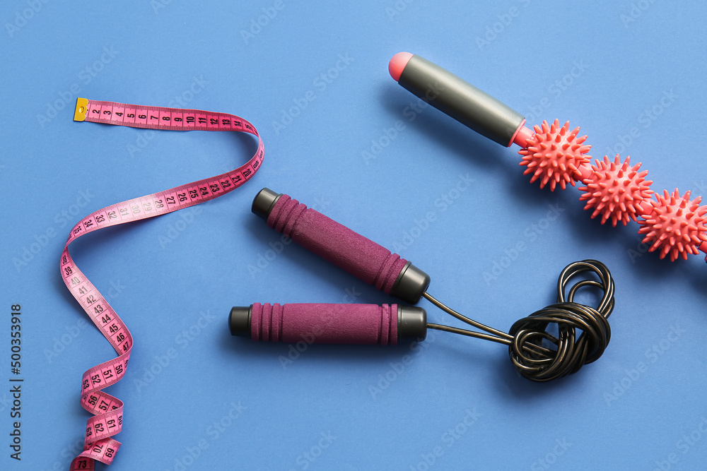 Skipping rope, measuring tape and massage roller on blue background