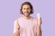 Handsome young man with tooth brush and paste on lilac background