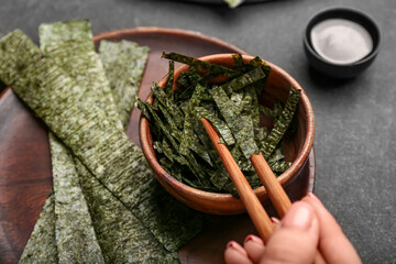 woman eating tasty seaweed sheets on black background, closeup