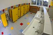 interior of bathrooms of a kindergarten with low sinks and yellow toilet cubicles without children
