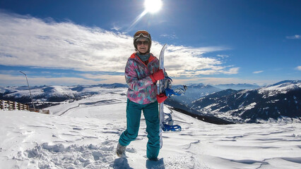 Wall Mural - A woman walking on powder snow with her snowboard on top of Katschberg in Austria. Panoramic view on the surrounding mountains. Winter wonderland. Sunny winter day. She is full of energy and happy