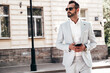 © halayalex - Portrait of handsome confident stylish hipster lambersexual model.Sexy modern man dressed in elegant white suit. Fashion male posing in the street background in Europe city at sunset. In sunglasses