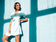 © halayalex - Young beautiful smiling female in trendy summer dress. Sexy carefree woman posing near blue wall in studio. Positive model having fun. Cheerful and happy. At sunny day. Shadow from window