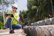 © kamonrat - Woman construction site engineer architect worker with hard hat using tablet for checking concret pipes