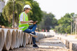 © kamonrat - Woman construction site engineer architect worker with hard hat using tablet for checking concret pipes