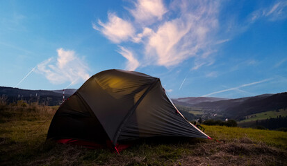 Tourist tent in the mountains under dramatic evening sky. Colorfull sunset in mountains. Camping travell concept. Traveler people enjoying the advanture alternative vacation