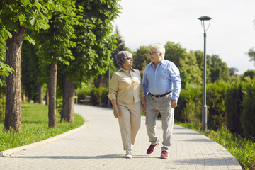 Staying in love is something very special. Cheerful senior couple having a good time in a city park walking, laughing and enjoying a sunny day. Mature family talking about something while walking.