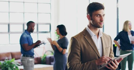 Poster - He takes his job very seriously. 4K video footage of a young man using a digital tablet while standing in a modern office with coworkers in the background.