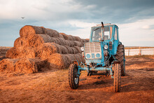 Retro Tractor Near Haystacks In The Countryside. Agricultural Equipment And Harvest Season