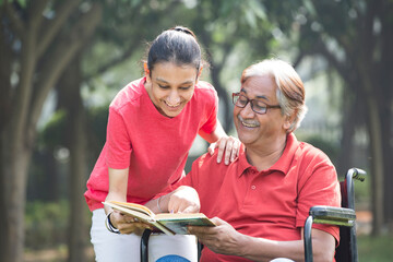 Happy grandfather in a wheelchair reading a book with granddaughter at park