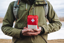 The Guy Holds In His Hands A Hiking Bag, A First Aid Kit With Medicines, A Red Emergency Bag Of First Aid. Medicines In A Package, Red Cross.