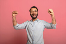 Lucky One. Excited Indian Guy Celebrating Victory And Gesturing YES With Fists Raised On Pink Background. Overjoyed Multiracial Bearded Man In Casual Jeans Shirt Winning