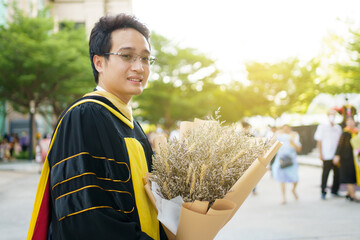 Happy Asian graduate student holding a beautiful bouquet of flowers in the university graduation ceremony. 
