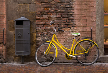 Old, yellow vintage bicycle against a textured, brick wall in Lucca, Italy
