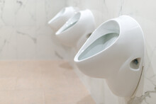 A Row Of Three Ceramic Urinals In The Marble Interior Of Public Toilets.