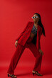 Elegant fashionable Black woman wearing classic red suit with blazer and trousers, zebra print top, trendy white frame sunglasses, strap sandals. Fashion full-length studio portrait 
