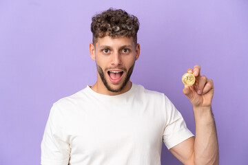 Wall Mural - Young caucasian man holding a Bitcoin isolated on purple background with surprise facial expression