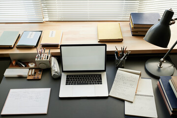 Above view of students desk with open laptop, sketchpads, office supplies, lamp and books on window sill