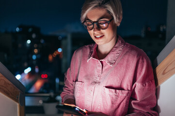 Woman using smartphone at night while standing near the window at home