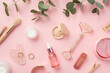 Top view photo of makeup brushes rose quartz roller gua sha pink eye patches glass bottles with serum cream eyeshadow lip gloss hairpins gold rings wristlet and eucalyptus on isolated pink background