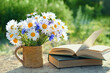 flowers bouqet in cup and old books on table in garden. rustic summer natural background. concept of reading, relaxation. summer season