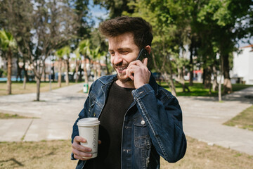 Wall Mural - Smiling young man, handsome man holding coffee cup making voice call, have a good and fun time