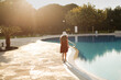 A child girl teenager in a casual dress with a hat walks near the pool in the evening at sunset.